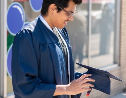 graduate in graduation gown holding hat