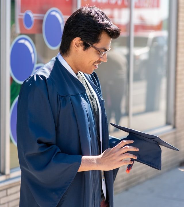 graduate in graduation gown holding hat